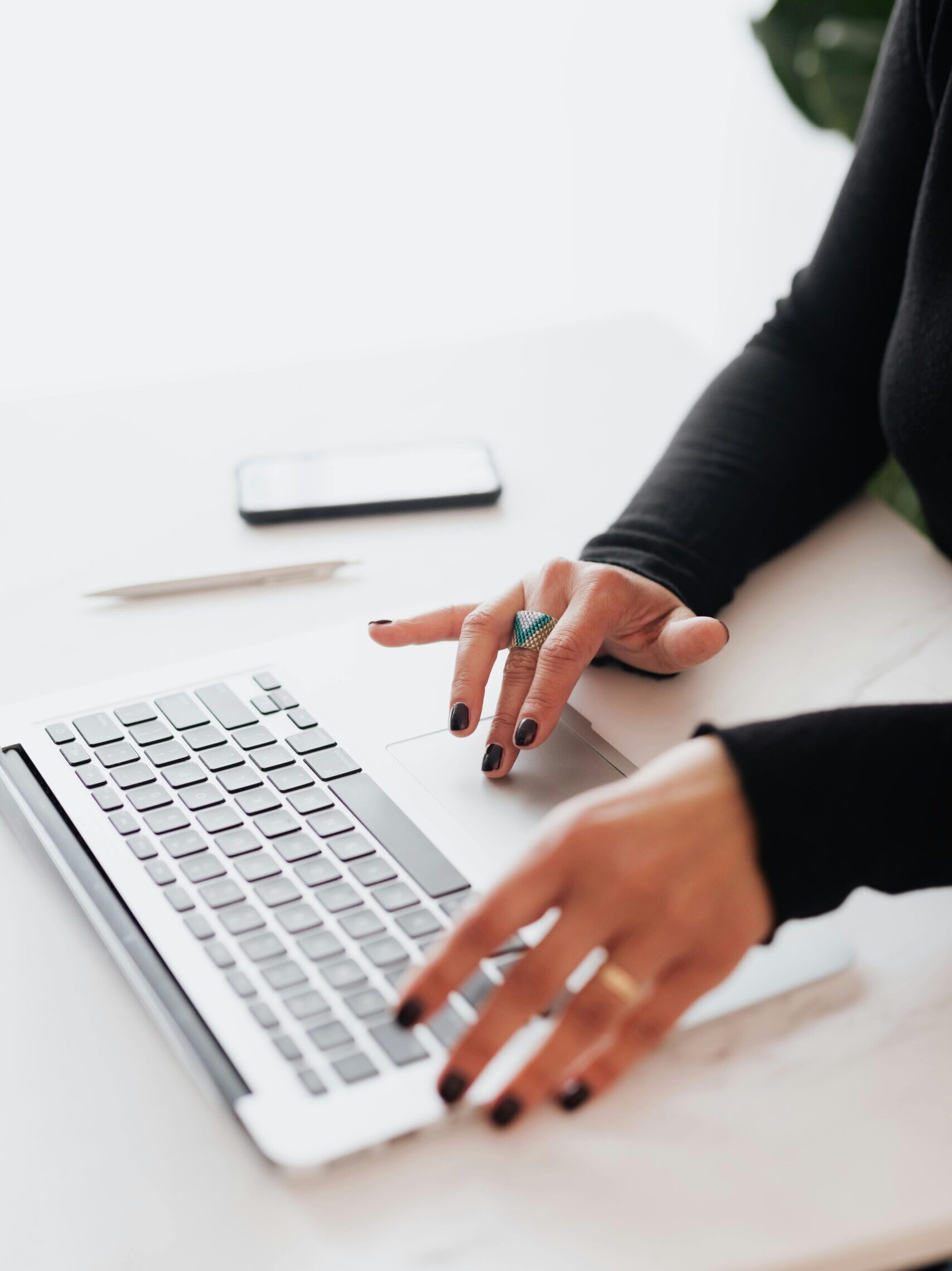 A businesswoman's hands typing on a laptop at a bright, modern workspace.
